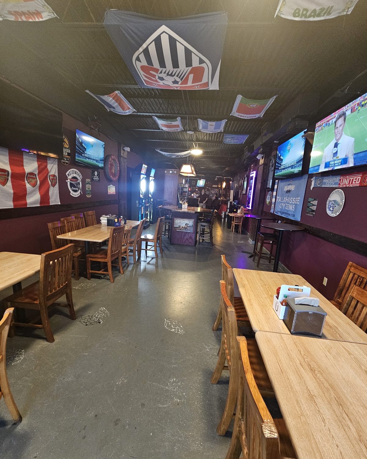 Long wooden tables down the middle of a dark red room, national flags and supporters’ club banners hanging overhead, televisions on both walls.
